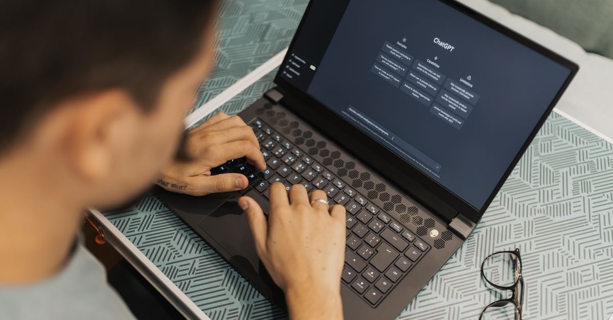 Man typing on a laptop showing the ChatGPT start screen, with glasses resting on a patterned table