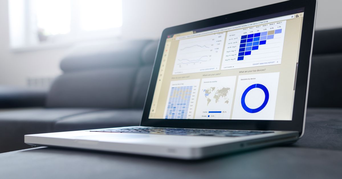 Open laptop on a dark sofa showing line charts, a world map and a donut graph on screen