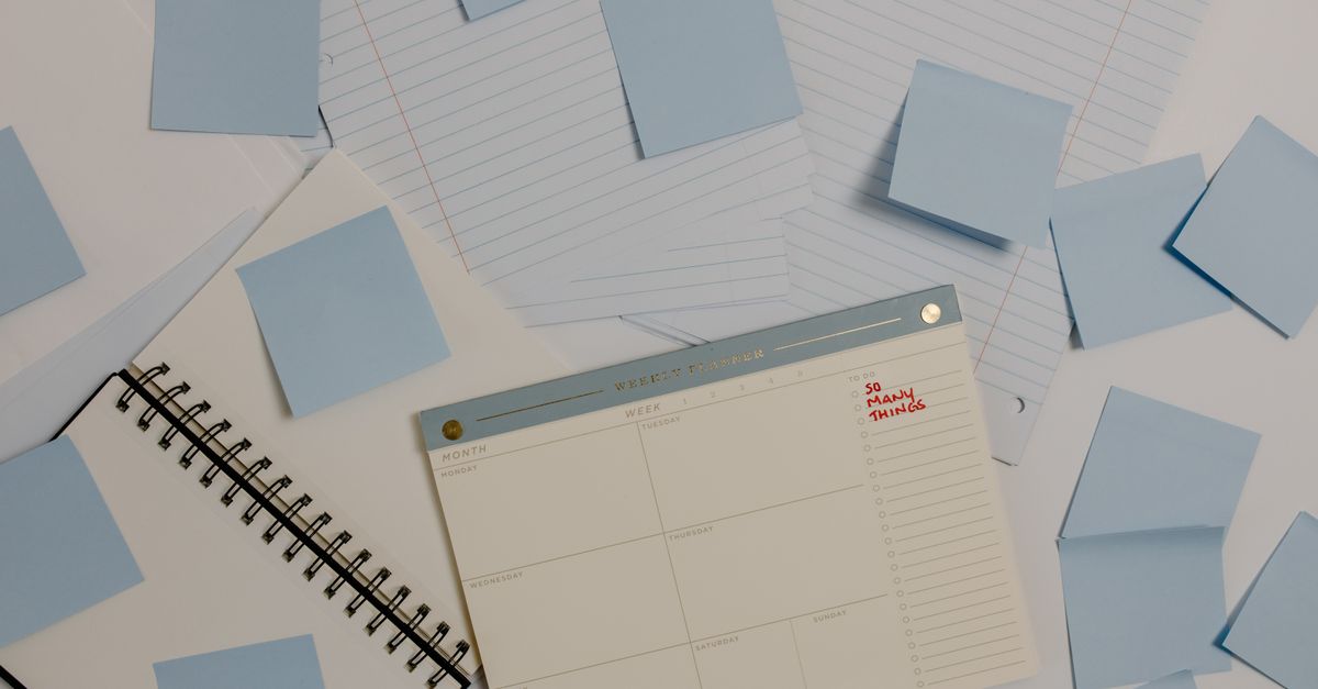 Desk planner, spiral notebook and light blue sticky notes spread across sheets of lined paper