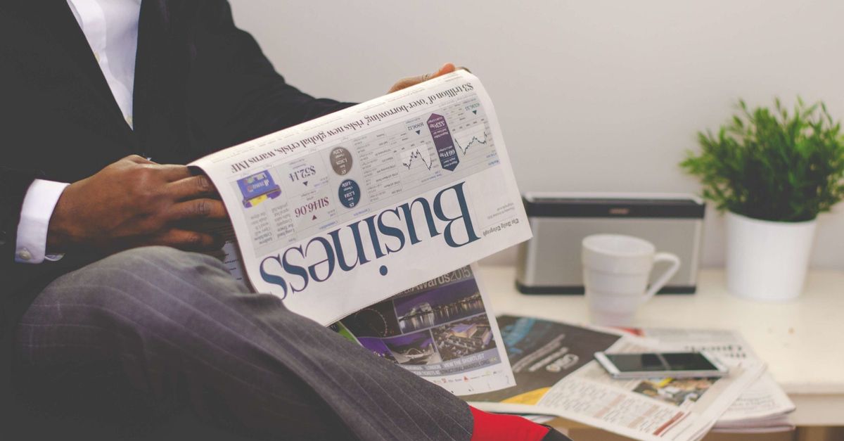 Man in a suit reading the business section of a newspaper beside a coffee mug and a plant
