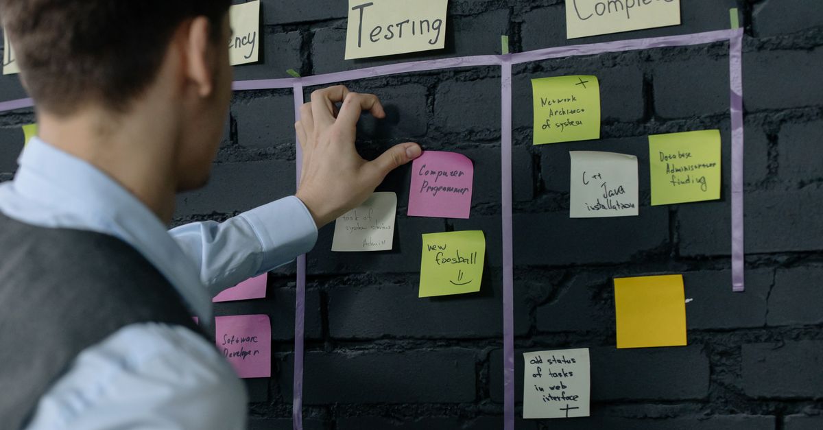 Man placing sticky notes on a wall task board with Testing and Complete columns